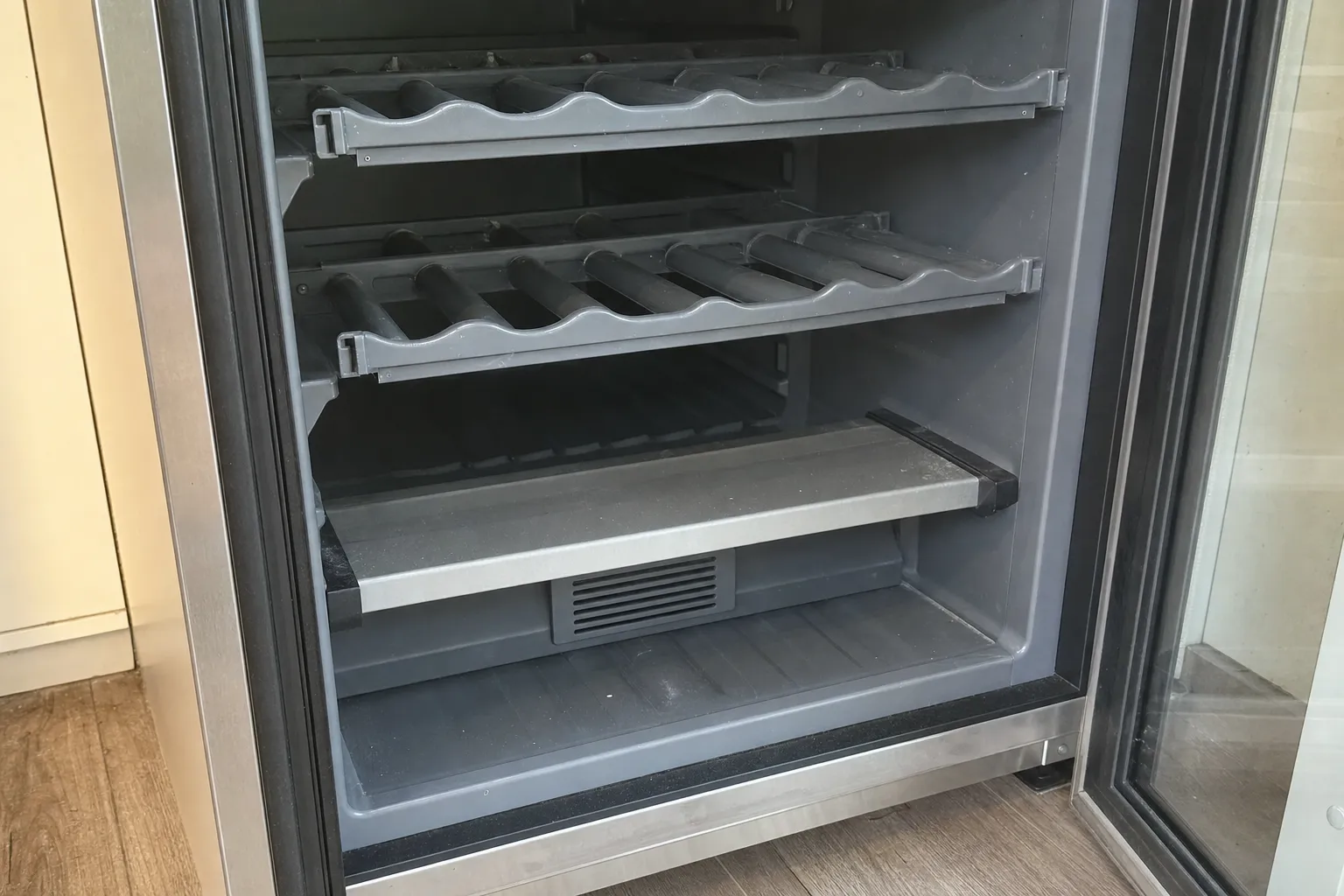 Empty wine cooler interior with contoured bottle shelves behind an open glass door